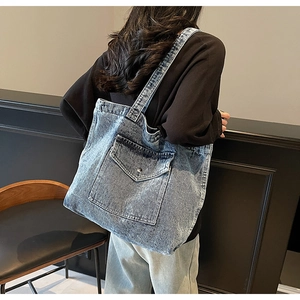 Detail of acid wash denim tote bag showing vintage texture and front flap pocket on a model