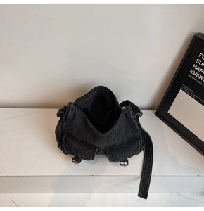 Detail view of washed black denim crossbody bag featuring multiple pockets and metal hardware