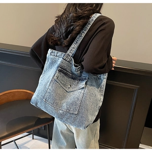 Detail of light blue washed denim tote bag with front pocket shown on a shoulder