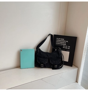 Detail view of black denim motorcycle bag with double buckle pockets and crescent shape
