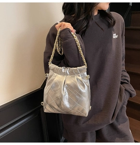 Detail of silver quilted bucket bag with metallic chain strap worn by a model