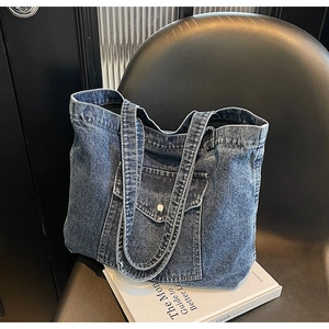 Detail of blue denim tote bag showing washed fabric texture and front pocket with buckle