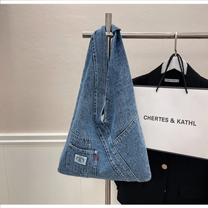 Detailed shot of a blue denim tote bag with a functional pocket and artistic woven patch