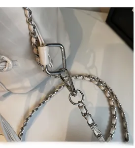 Detailed macro view of silver metal square buckle and lobster clasp on white leather bag