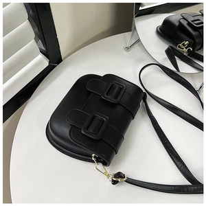Détail d'un sac besace vintage noir avec boucles dorées sur fond de table blanche