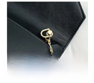 Détails rapprochés de l'anneau en D doré et de la chaîne sur un sac enveloppe en cuir noir