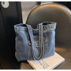 Close-up of blue denim tote bag with metal button pocket detail on black chair