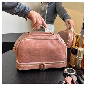 Detail view of pink leather makeup bag with dual zippers and handle on dark wood surface