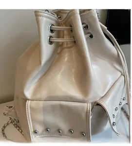 Close-up of creamy white drawstring bucket bag with silver rivets and polished texture