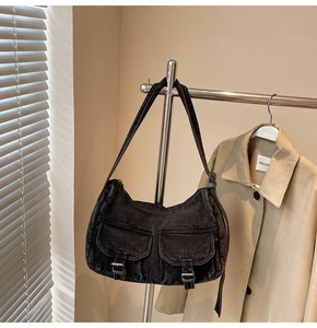 Close-up of black denim biker bag featuring vintage metal buckles and dual front pockets