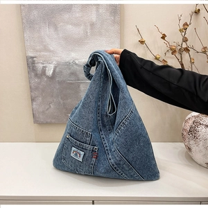 Detail of blue washed denim hobo bag featuring wide knotted strap and graphic fabric patch