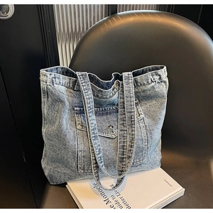 Close-up of washed blue denim tote bag with metal button pocket and thick fabric texture