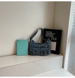Close-up of vintage blue denim hobo bag with dual cargo pockets on a white marble table