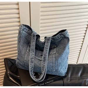Detail view of washed blue denim tote bag with front flap pocket and dual long handles