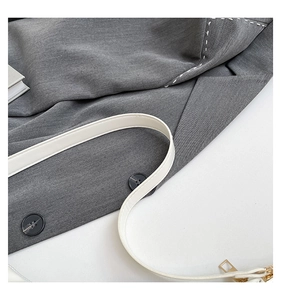 Detail of white leather strap with golden zipper and contrast stitching on grey suit fabric