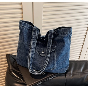 Detailed view of dark blue denim tote bag featuring front pocket and silver metal buckle