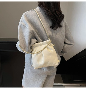 Detail of creamy white quilted bucket bag with glossy finish and gold metal chain strap