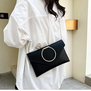 Détail d'une pochette en cuir PU noir avec un grand anneau doré et une bandoulière en chaîne