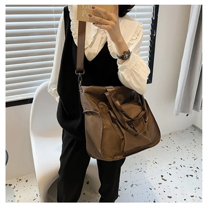Detail of a large brown nylon tote bag featuring front pocket and canvas shoulder straps