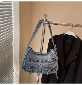 Detail of light blue washed denim shoulder bag with dual utility pockets and metal buckles