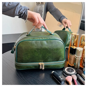 Detail view of large dark green vintage leather makeup bag with dual zipper on vanity
