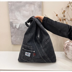 Detail of washed black denim bag with decorative white stitching and a small front pocket