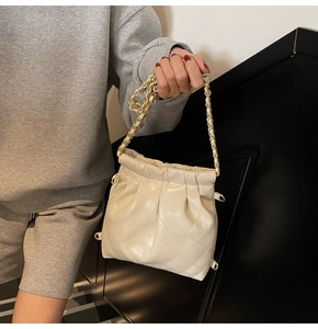 Detail of cream quilted bucket bag with drawstring closure and golden chain strap
