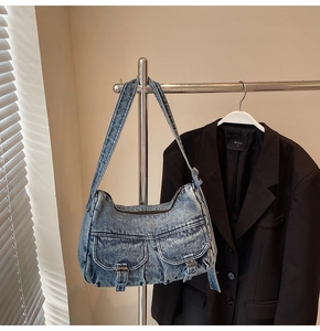 Detail showing two front pockets with metal buckles on a blue wash denim shoulder bag