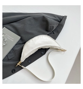 Detail shot of a minimalist white leather crescent bag with golden hardware and zipper