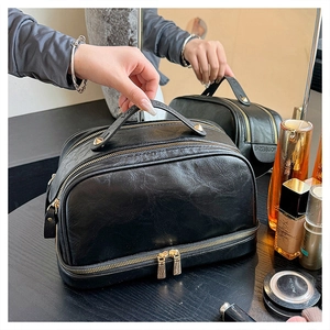 Close-up of black double-layer faux leather makeup bag with gold zippers and handle