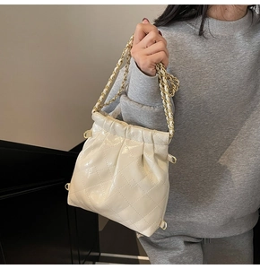 Detail of quilted creamy white bucket bag with glossy finish and gold chain strap