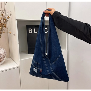 Close-up of hobo denim bag featuring a front pocket with red stitching and graphic label