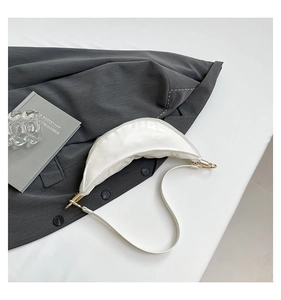 Detail of a white crescent shoulder bag with glossy texture on a grey suit background
