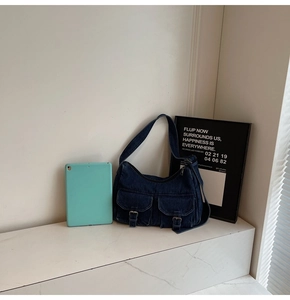 Detailed close-up of dark blue denim shoulder bag with dual front buckle pockets