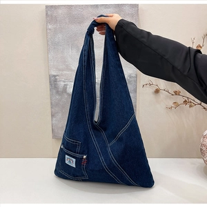 Detailed close-up of dark blue denim hobo bag with white stitching and knot handle detail