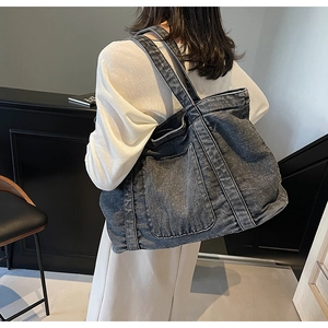 Detail view of large washed black denim tote bag featuring a spacious front pocket and sturdy straps
