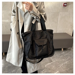 Detail of large black nylon tote bag with front pocket and decorative chain on a model