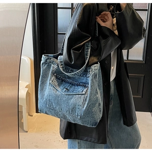 Side view of large washed blue denim tote bag with front pocket shown on a model