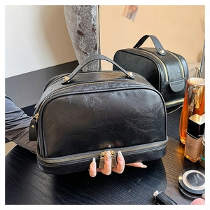 Detail view of black dual-layer leather toiletry bag with gold zippers and litchi texture