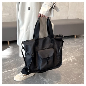 Detail view of large black nylon tote bag with front pocket and adjustable shoulder strap