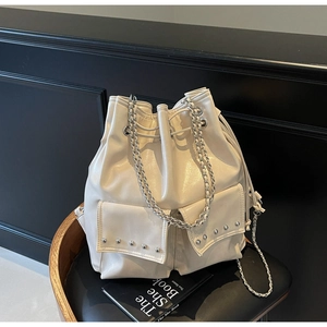 Detail of a creamy white bucket bag with silver studs and chain straps in a dark setting