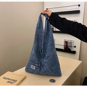 Detail of blue denim hobo bag featuring a small pocket with a colorful rainbow logo label