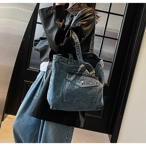Detail of vintage denim tote bag showing front pocket and stitching on a model