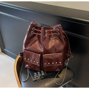 Detail of burgundy drawstring bucket bag featuring silver rivets and chain strap