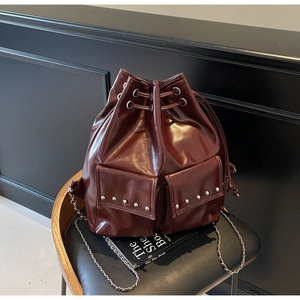 Detail of burgundy bucket bag with silver studs and chain strap on leather chair