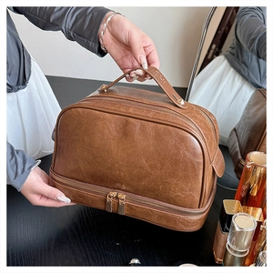 Close-up of vintage brown leather makeup bag showing dual zipper design and hand strap