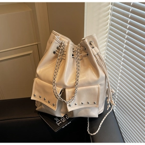Detail of cream drawstring bucket bag showing rivets, flip pockets and silver chain straps