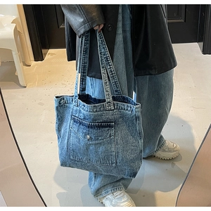 Close-up of vintage blue denim tote bag with front pocket detail worn by a model