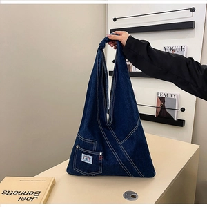 Close-up of deep blue denim shoulder bag with triangular silhouette and outer pocket
