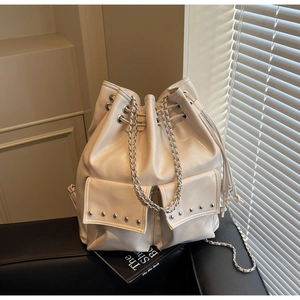 Detail of off-white bucket bag with silver rivet studs and drawstring on leather sofa